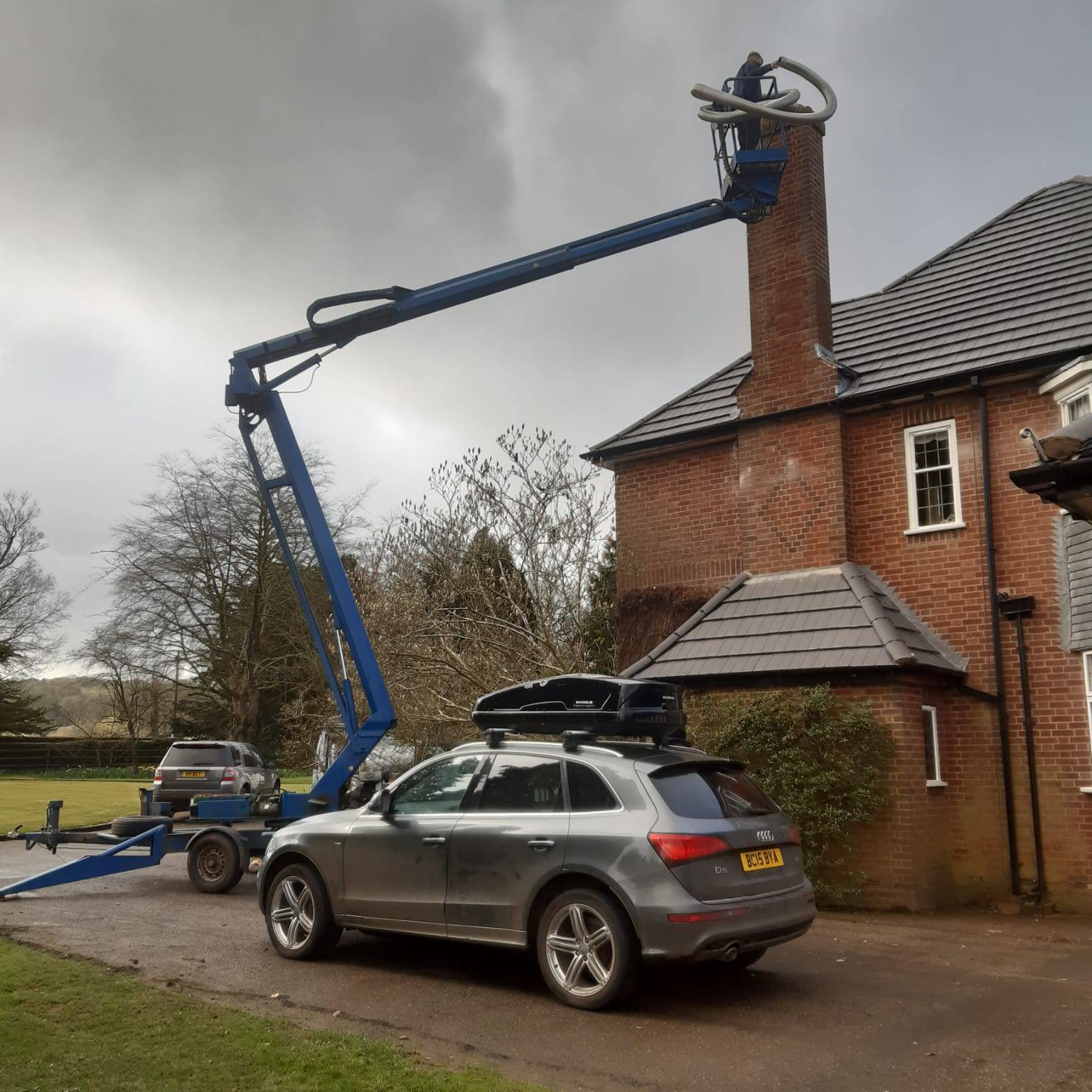 Photo of a man in a cherry picker reaching the chimney of a roof on a two storey building